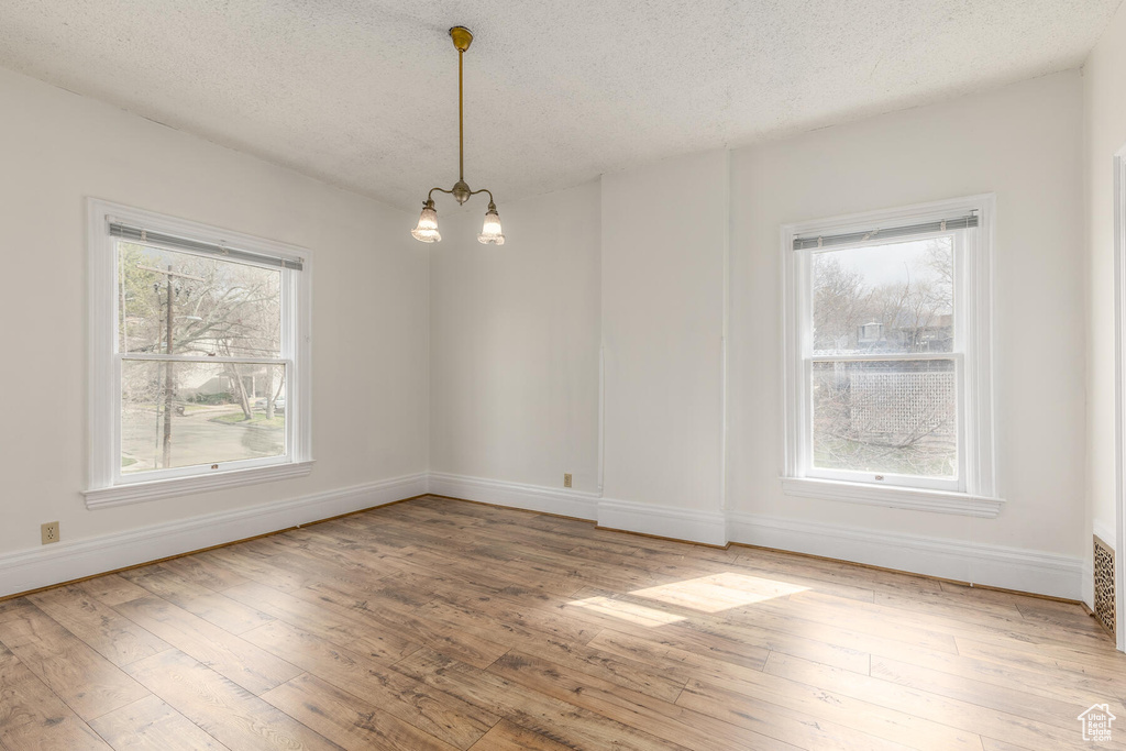 Spare room with a wealth of natural light, light hardwood / wood-style flooring, and an inviting chandelier
