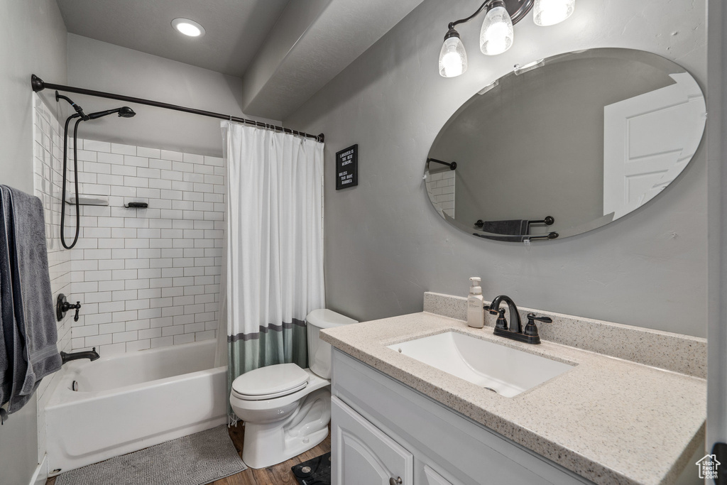 Full bathroom with toilet, large vanity, hardwood / wood-style floors, and shower / tub combo