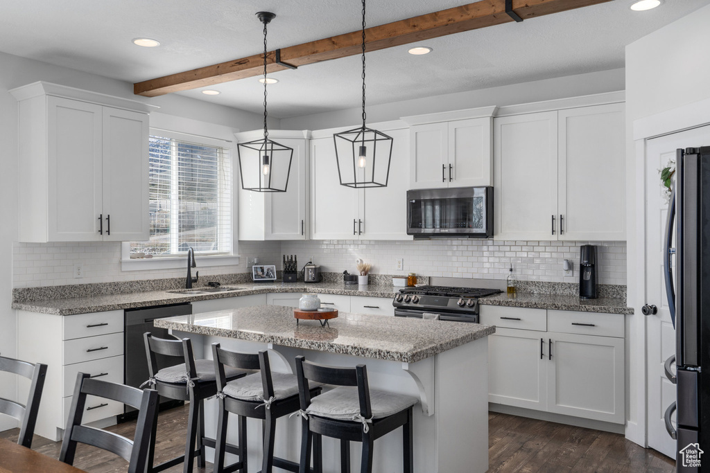 Kitchen with dark hardwood / wood-style flooring, white cabinets, appliances with stainless steel finishes, and beamed ceiling