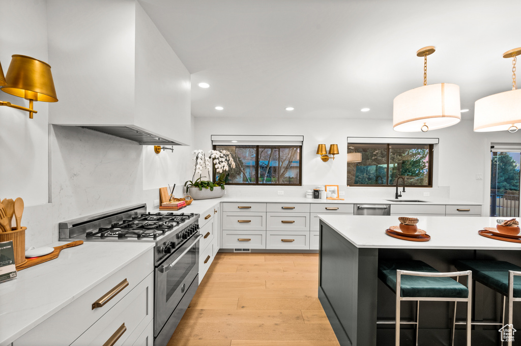 Kitchen featuring sink, appliances with stainless steel finishes, a breakfast bar area, light hardwood / wood-style floors, and white cabinetry