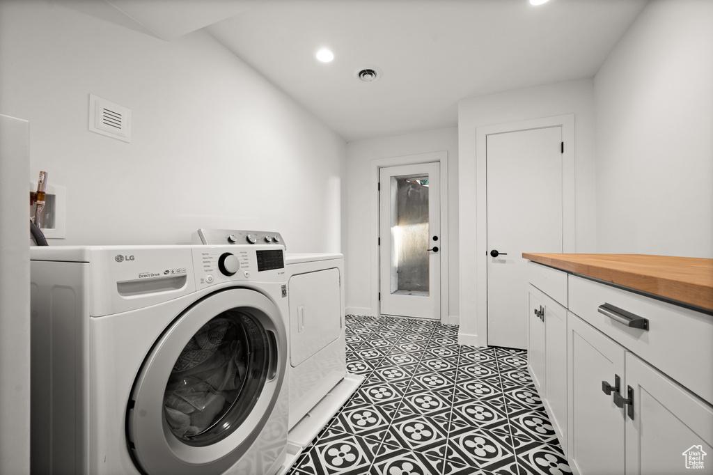 Clothes washing area featuring dark tile floors, cabinets, and washer and clothes dryer