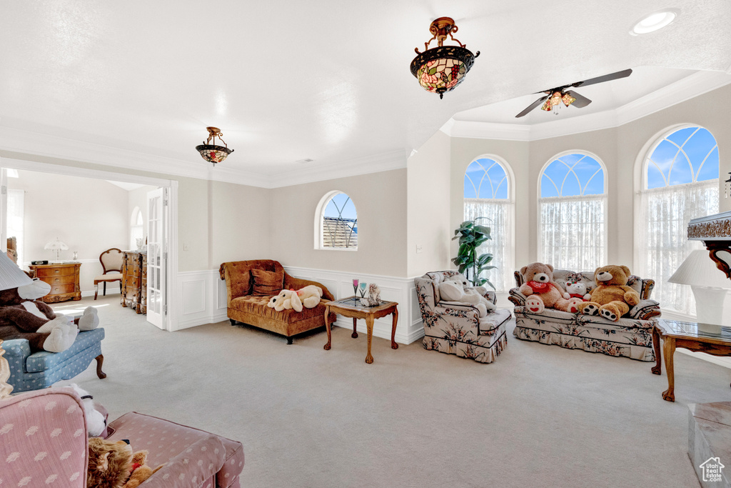 Living room with light carpet, a raised ceiling, ornamental molding, and ceiling fan
