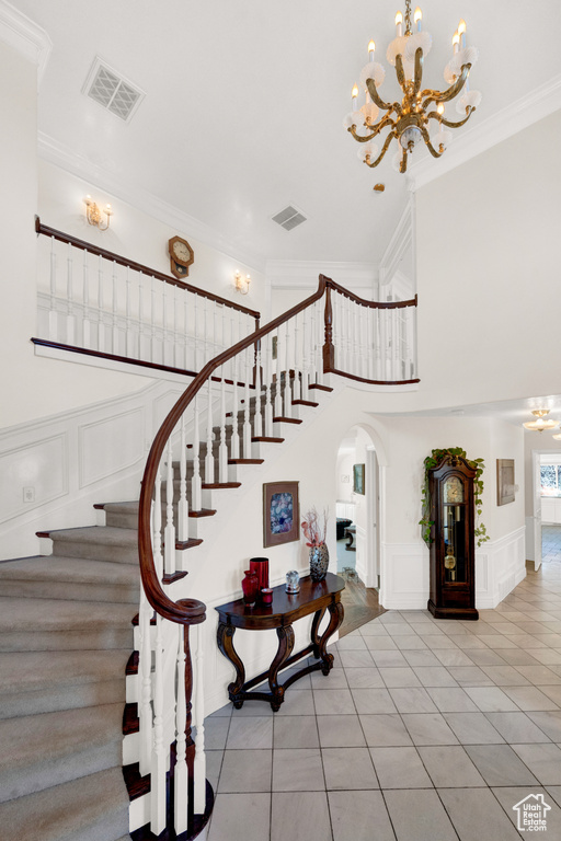 Stairs with an inviting chandelier, ornamental molding, and light tile floors