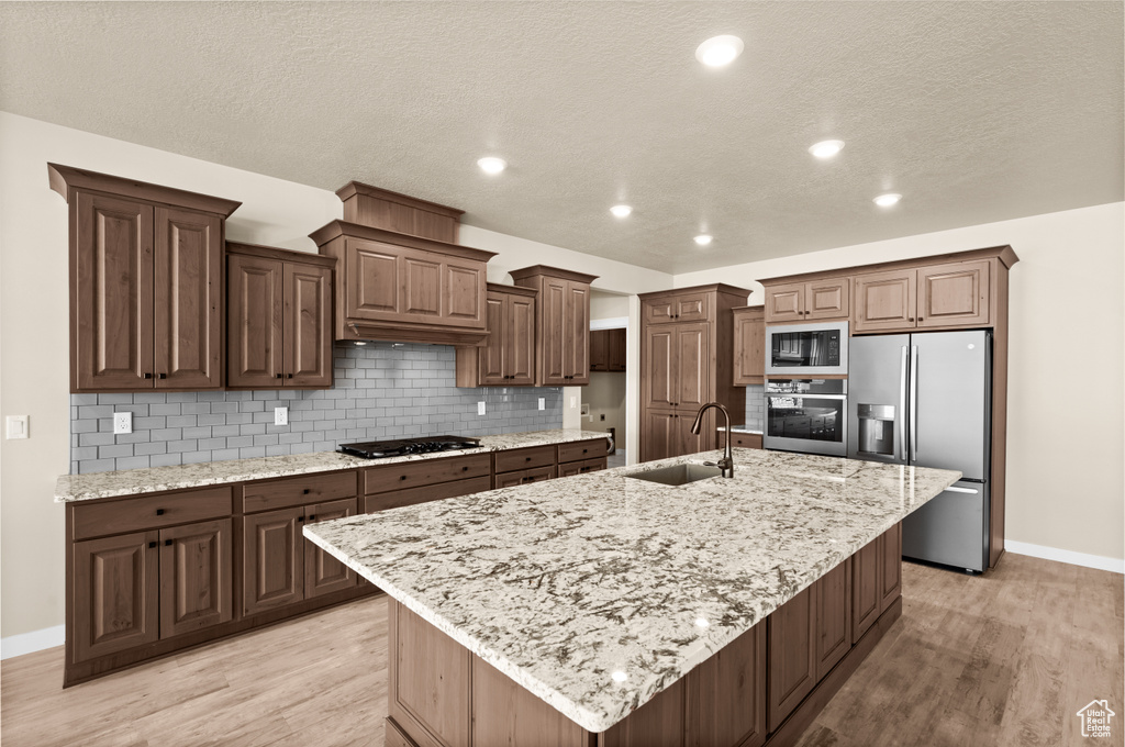Kitchen featuring an island with sink, sink, backsplash, light hardwood / wood-style floors, and black appliances