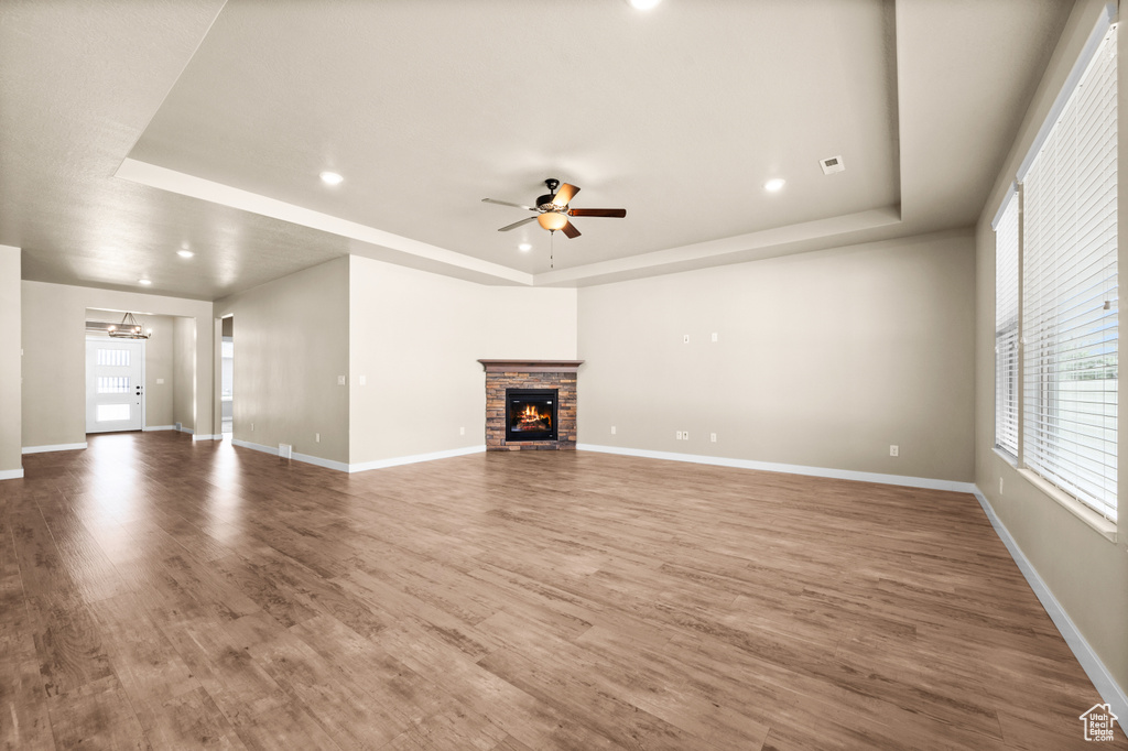 Unfurnished living room featuring dark hardwood / wood-style floors, ceiling fan, a fireplace, and a tray ceiling