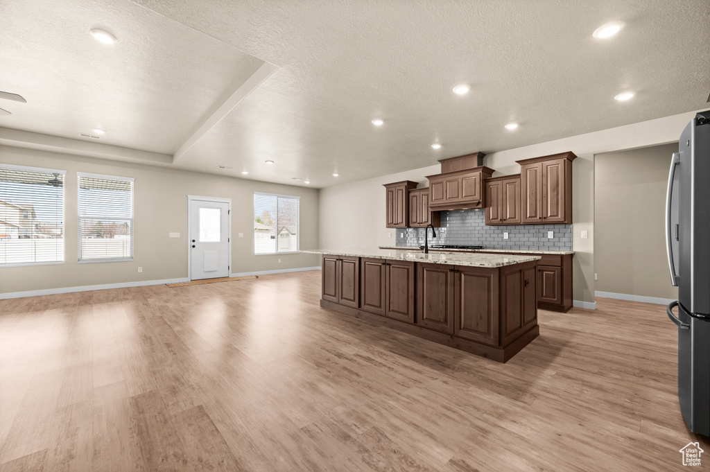 Kitchen with stainless steel refrigerator, light hardwood / wood-style floors, tasteful backsplash, and an island with sink