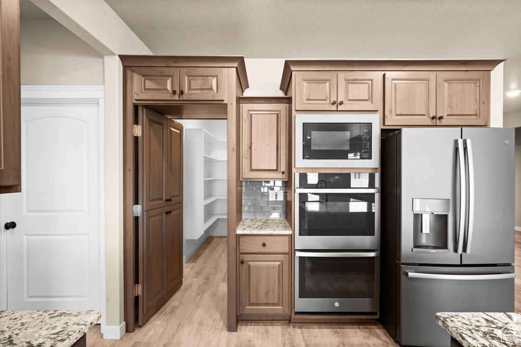 Kitchen with light hardwood / wood-style flooring, stainless steel appliances, tasteful backsplash, and light stone counters