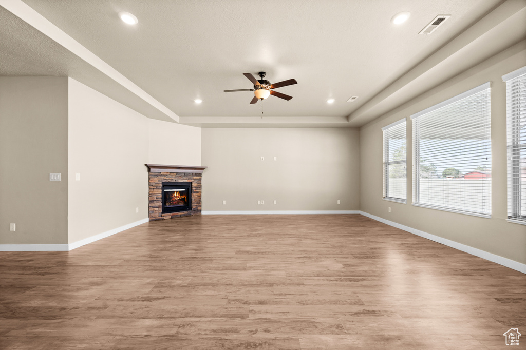 Unfurnished living room with ceiling fan, a fireplace, light wood-type flooring, and a raised ceiling