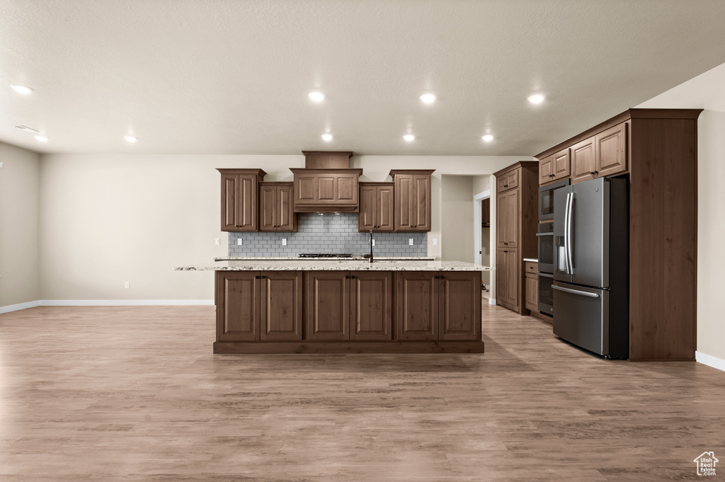 Kitchen with a kitchen island with sink, tasteful backsplash, stainless steel appliances, and light hardwood / wood-style flooring