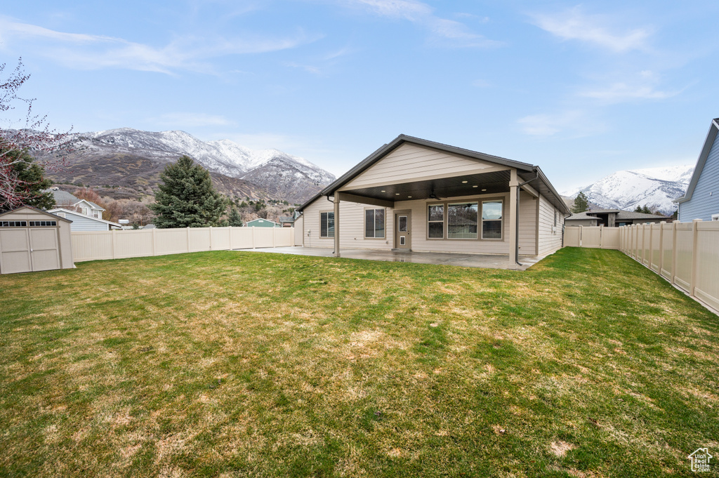 Rear view of house with a mountain view, a storage shed, a lawn, and a patio area