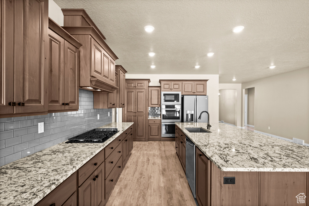 Kitchen with a center island with sink, stainless steel appliances, sink, and light hardwood / wood-style flooring