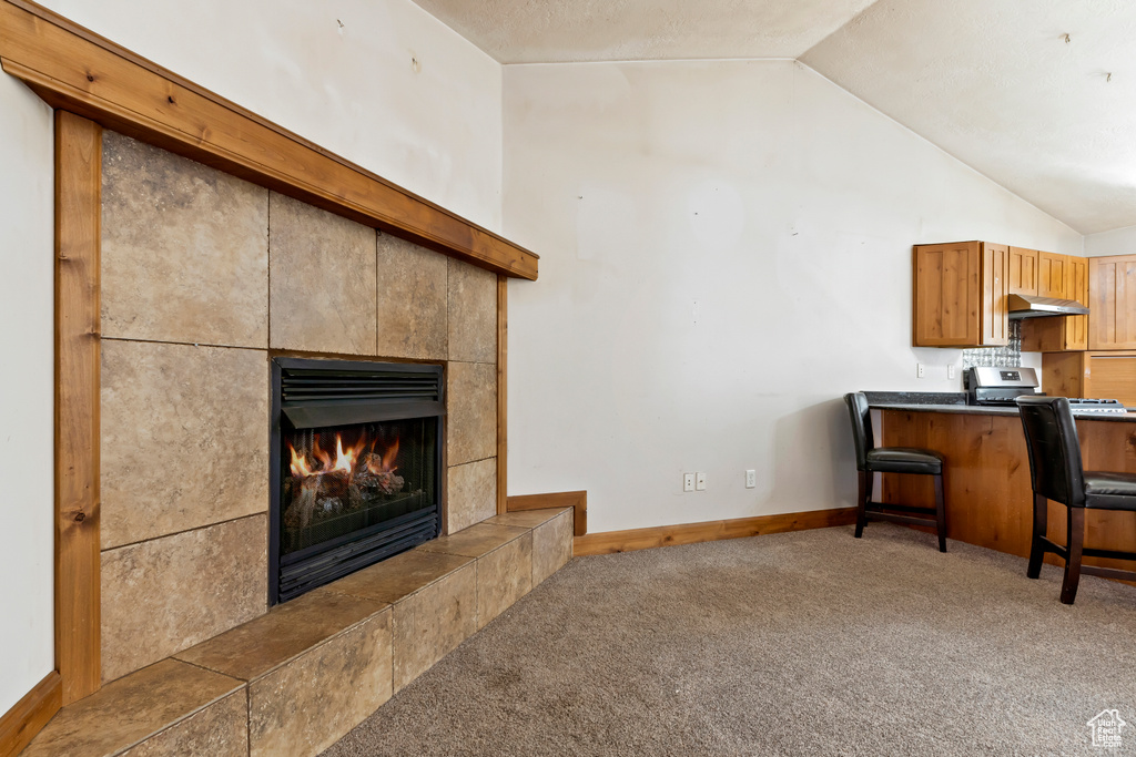 Carpeted living room featuring lofted ceiling and a tiled fireplace