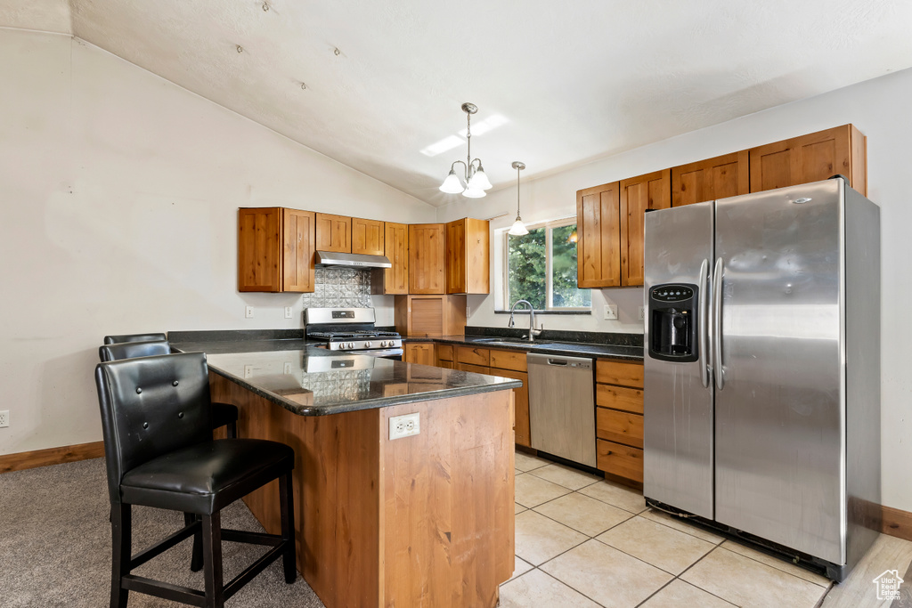 Kitchen with appliances with stainless steel finishes, hanging light fixtures, vaulted ceiling, a kitchen breakfast bar, and sink
