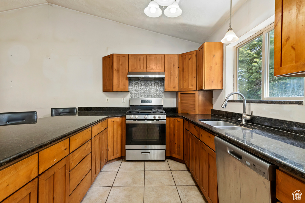 Kitchen featuring decorative light fixtures, stainless steel appliances, lofted ceiling, sink, and light tile floors