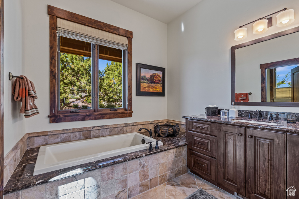 Bathroom featuring a relaxing tiled bath, vanity with extensive cabinet space, and tile flooring