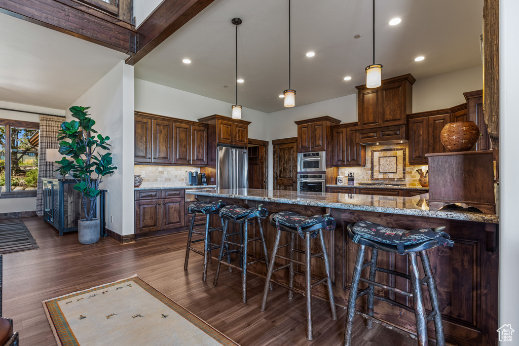 Kitchen featuring stone counters, backsplash, dark hardwood / wood-style floors, a kitchen bar, and stainless steel appliances