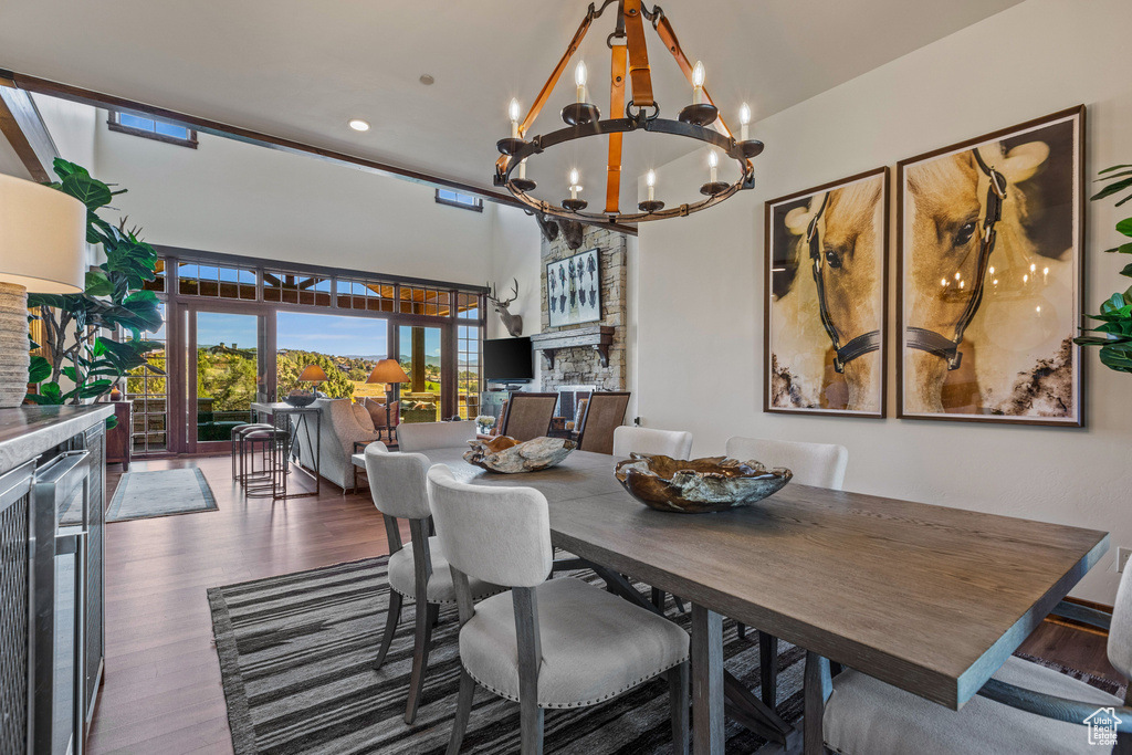 Dining area featuring an inviting chandelier, a stone fireplace, dark hardwood / wood-style floors, and a high ceiling