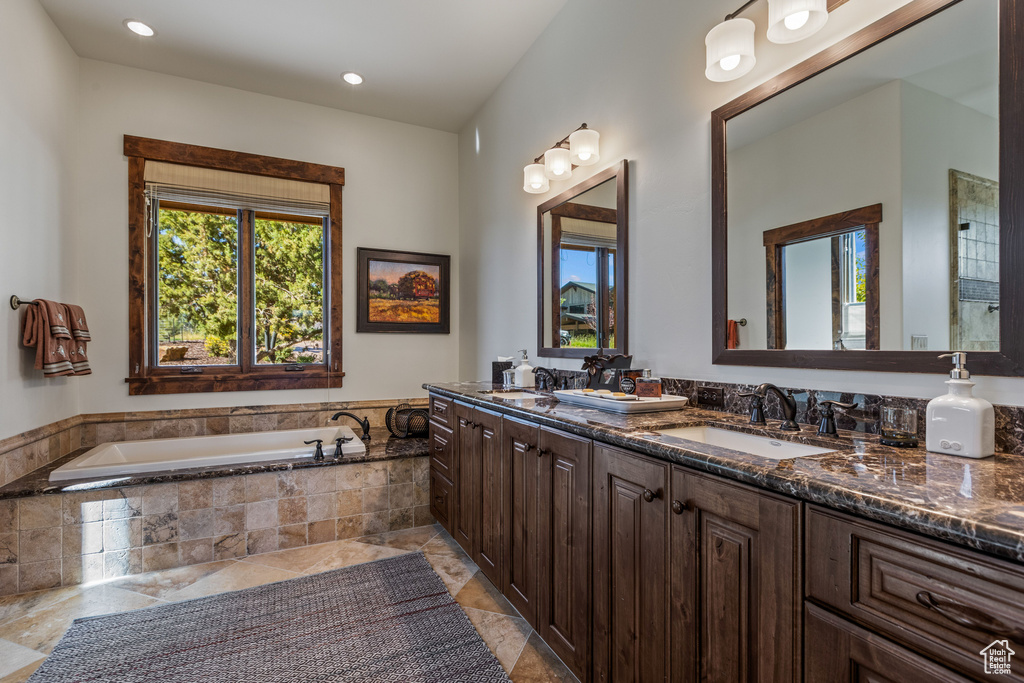 Bathroom featuring vanity with extensive cabinet space, dual sinks, tile floors, and tiled tub