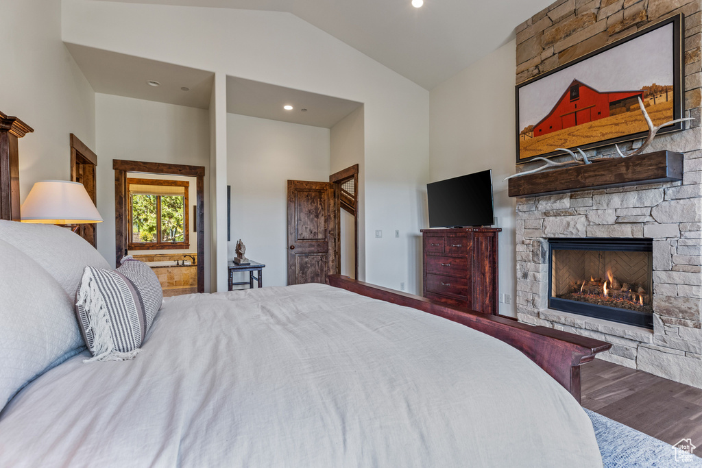 Bedroom with lofted ceiling, a stone fireplace, and wood-type flooring