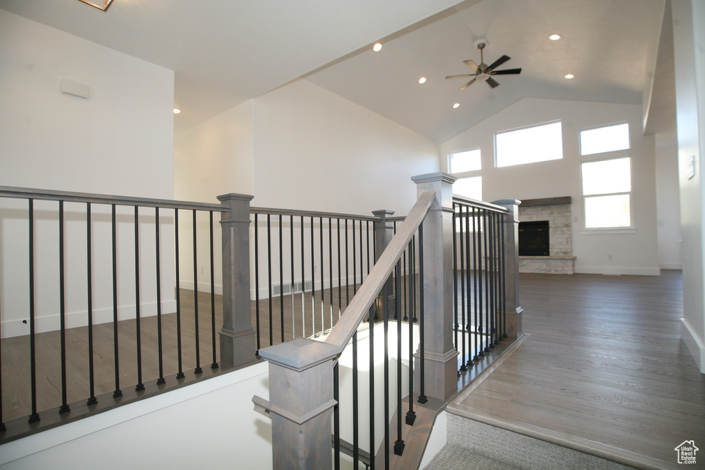 Staircase featuring a stone fireplace, dark hardwood / wood-style floors, ceiling fan, and high vaulted ceiling