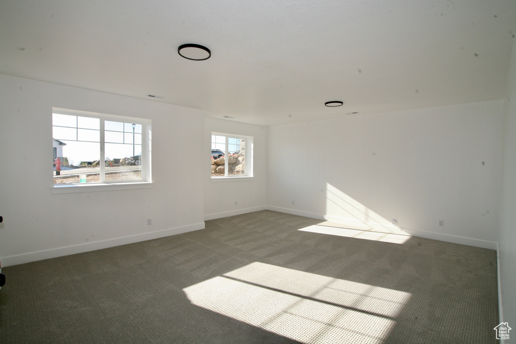 Unfurnished room featuring dark colored carpet and a wealth of natural light
