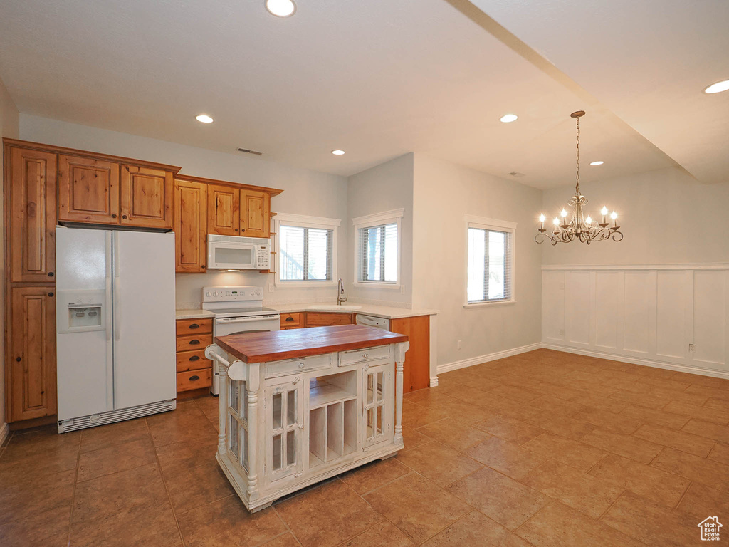 Kitchen featuring butcher block counters, white appliances, light tile floors, sink, and a chandelier