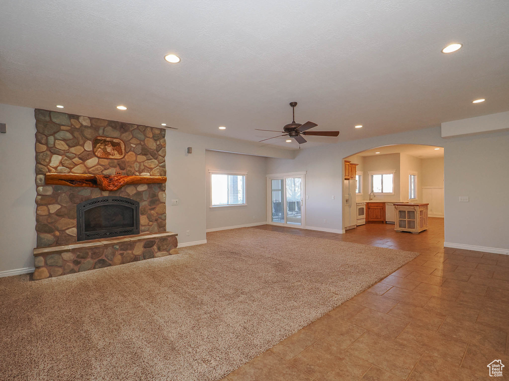 Unfurnished living room featuring ceiling fan, light colored carpet, and a stone fireplace