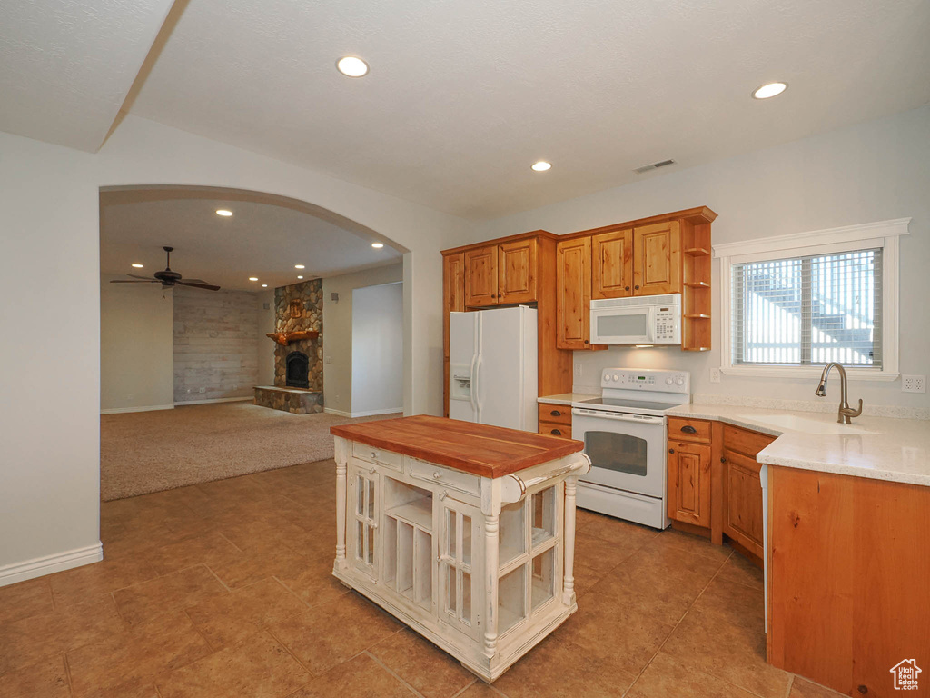 Kitchen featuring light colored carpet, a stone fireplace, ceiling fan, white appliances, and sink