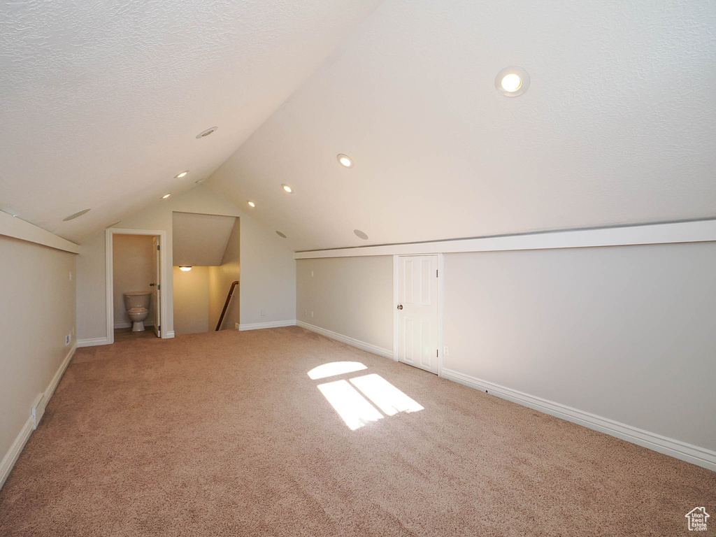 Bonus room with a textured ceiling, light colored carpet, and vaulted ceiling