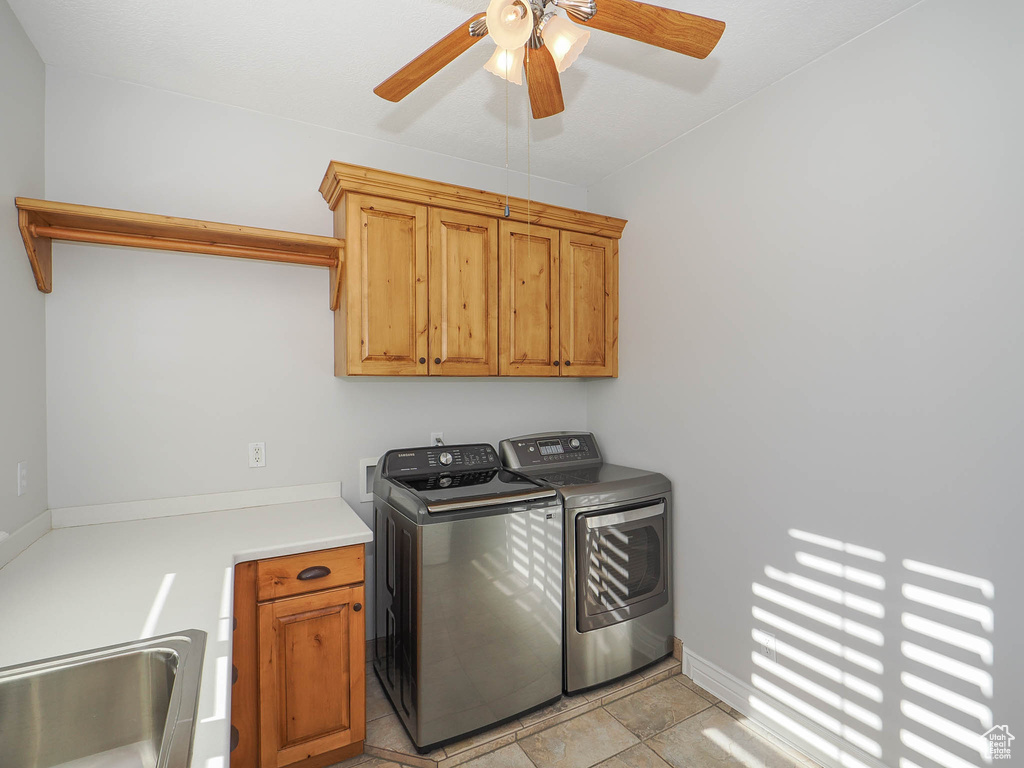 Laundry area with ceiling fan, light tile floors, sink, washing machine and dryer, and cabinets