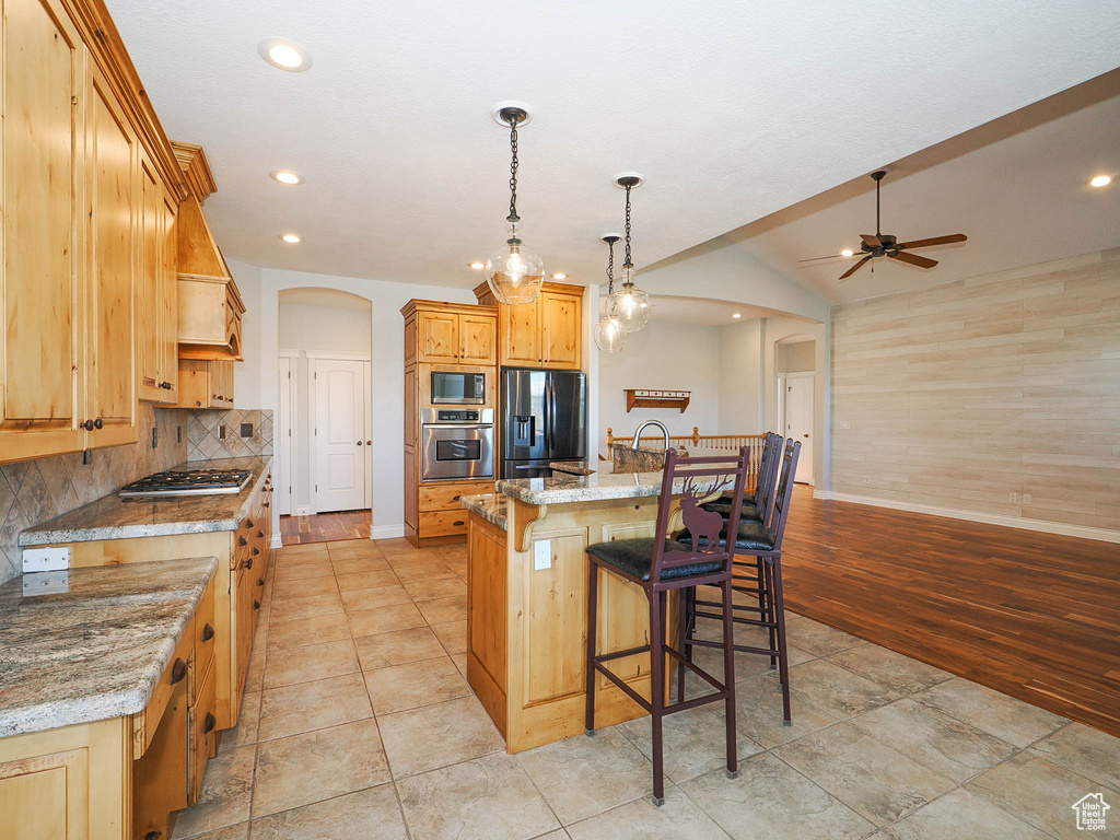 Kitchen featuring ceiling fan, light hardwood / wood-style floors, stainless steel appliances, an island with sink, and light stone counters