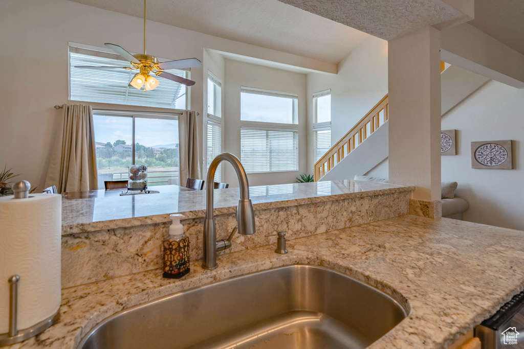 Interior space with a textured ceiling, ceiling fan, sink, and light stone countertops
