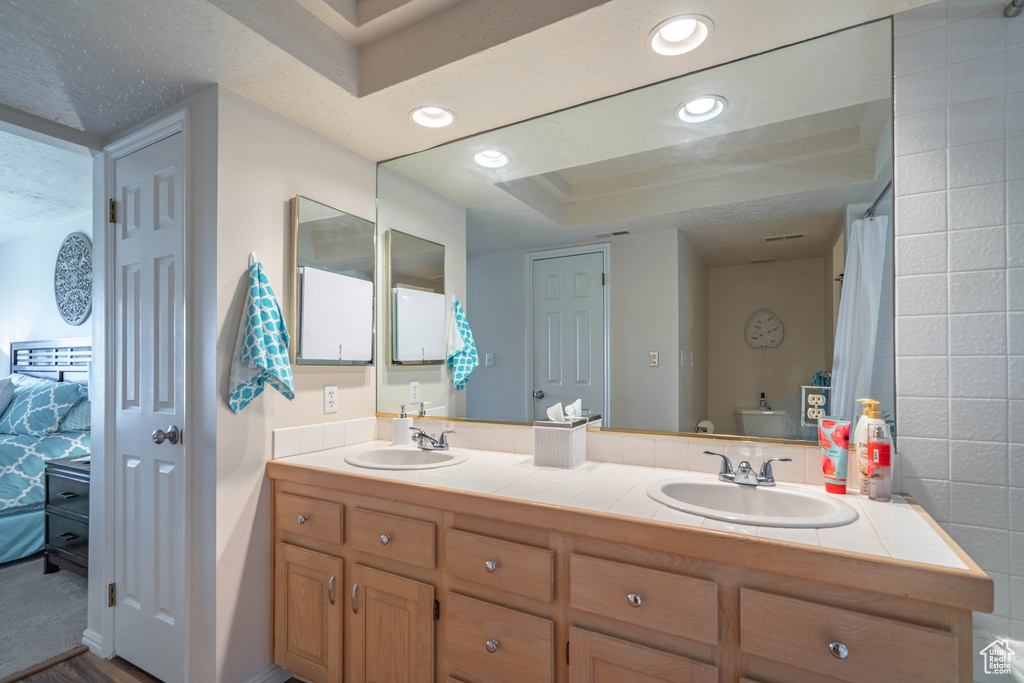 Bathroom with a raised ceiling, tile walls, dual sinks, and oversized vanity