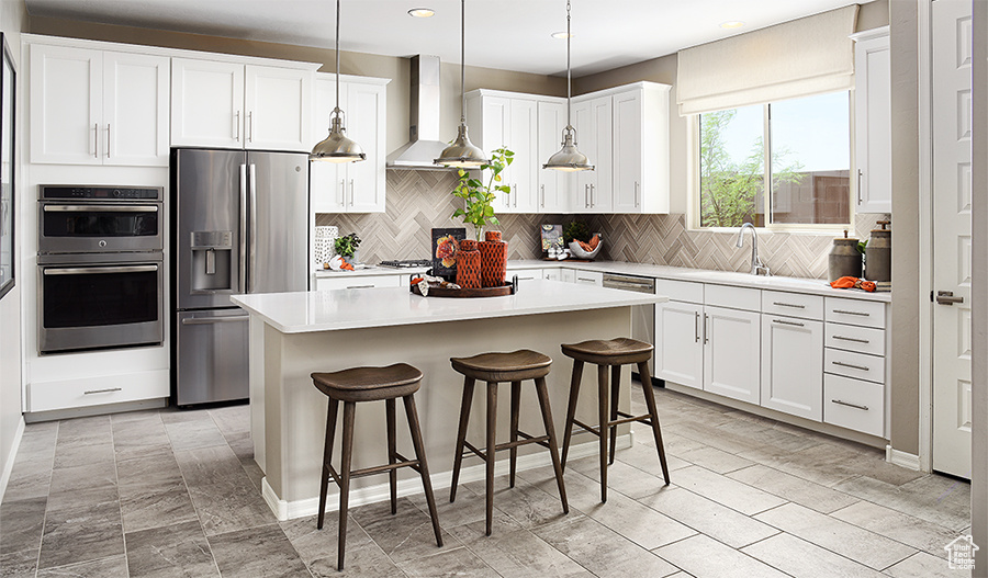 Kitchen with wall chimney exhaust hood, white cabinetry, appliances with stainless steel finishes, and a center island