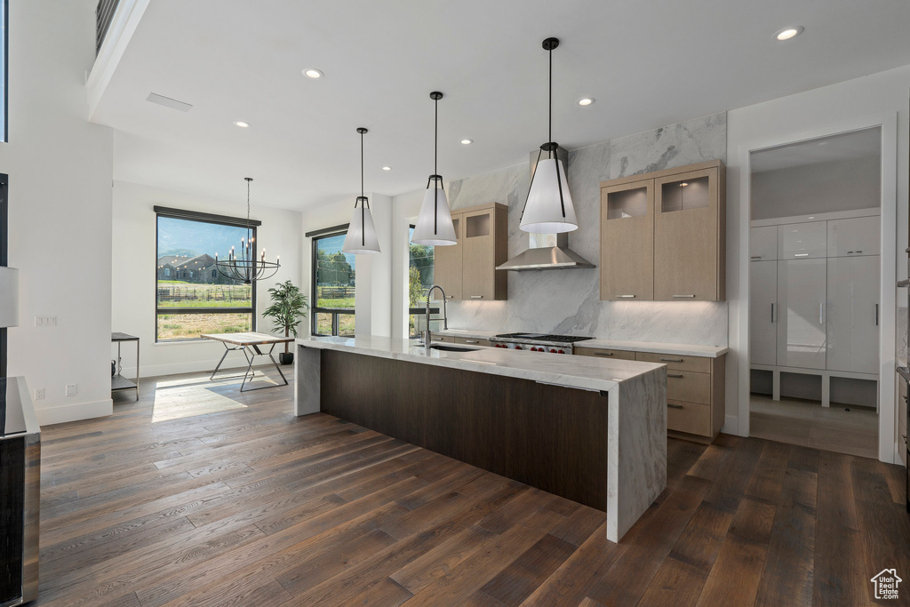 Kitchen featuring an island with sink, pendant lighting, sink, dark wood-type flooring, and an inviting chandelier
