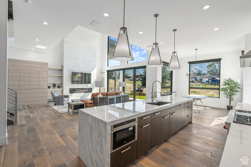 Kitchen with hanging light fixtures, dark hardwood / wood-style floors, light stone counters, and an island with sink