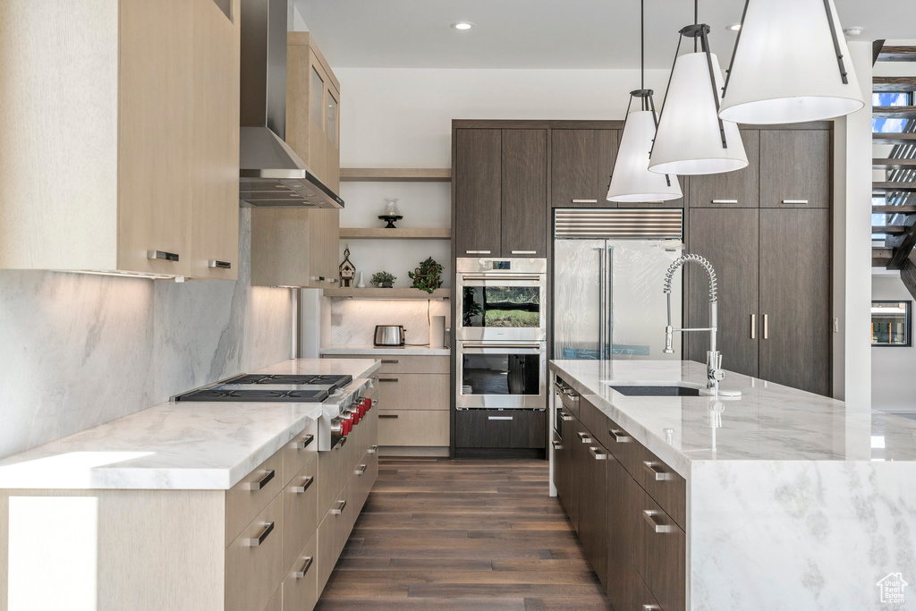 Kitchen featuring pendant lighting, tasteful backsplash, dark wood-type flooring, stainless steel appliances, and wall chimney exhaust hood