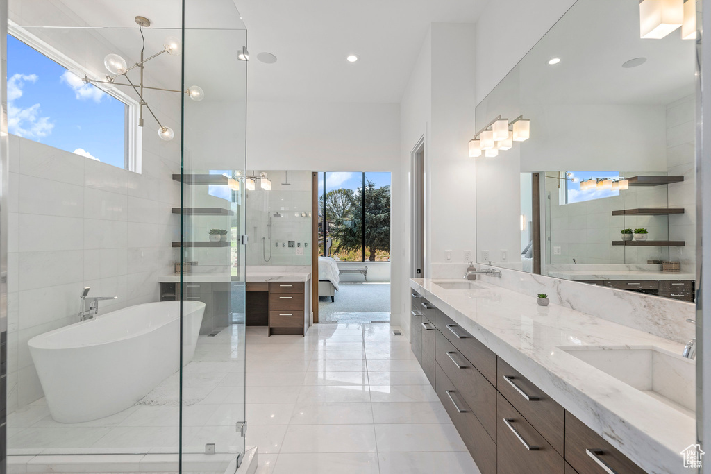 Bathroom with tile flooring, tile walls, a bath to relax in, double vanity, and a chandelier