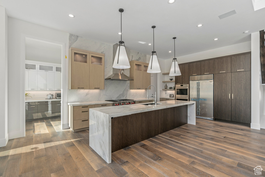 Kitchen featuring dark wood-type flooring, an island with sink, stainless steel appliances, pendant lighting, and sink