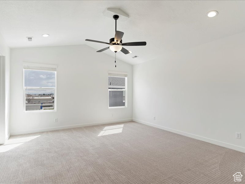 Empty room with ceiling fan, lofted ceiling, and light carpet