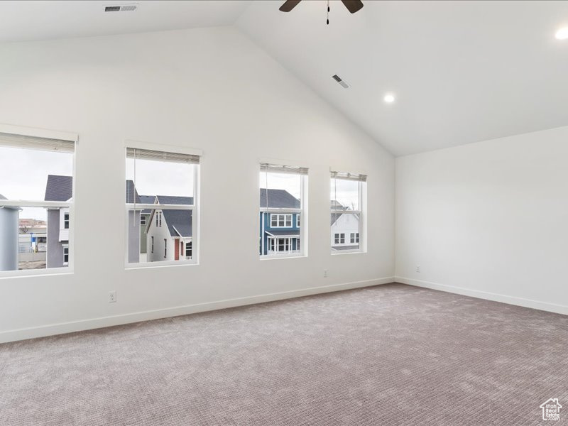 Carpeted empty room with high vaulted ceiling and ceiling fan