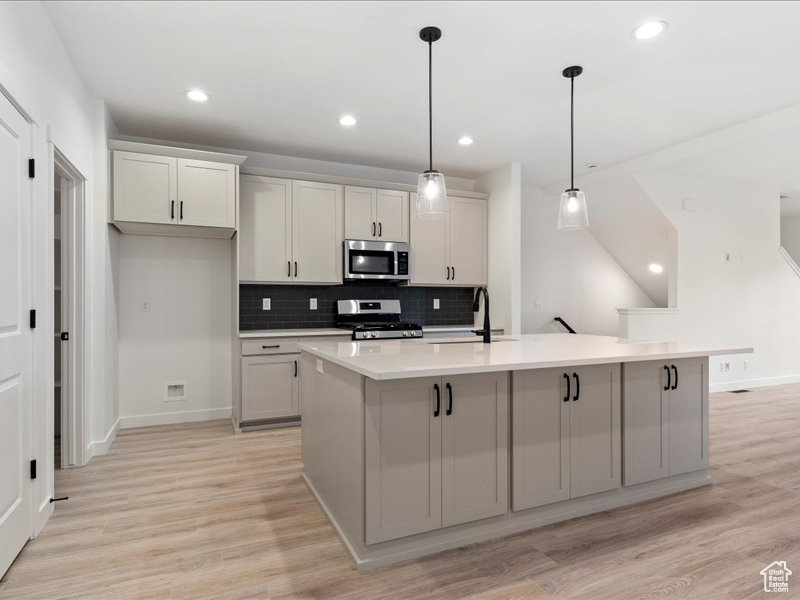 Kitchen with pendant lighting, stainless steel appliances, a kitchen island with sink, and light wood-type flooring