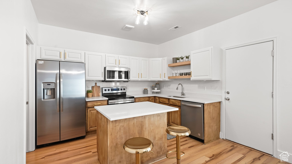 Kitchen with light hardwood / wood-style flooring, stainless steel appliances, backsplash, and a kitchen island