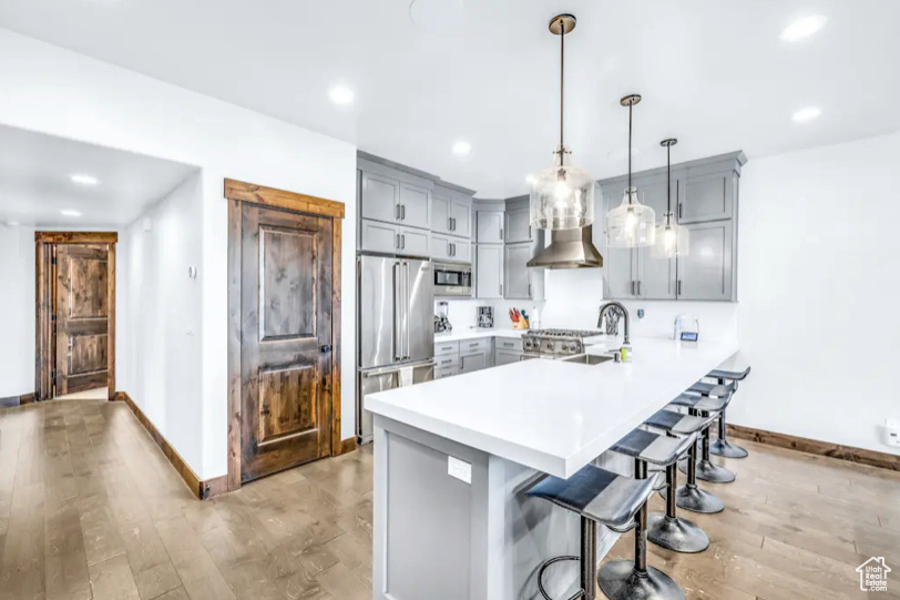 Kitchen featuring appliances with stainless steel finishes, hanging light fixtures, a breakfast bar, kitchen peninsula, and light hardwood / wood-style flooring