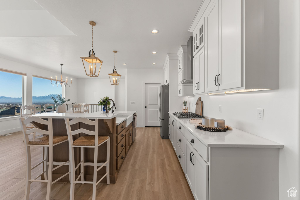 Kitchen featuring appliances with stainless steel finishes, light hardwood / wood-style flooring, white cabinets, a center island with sink, and pendant lighting
