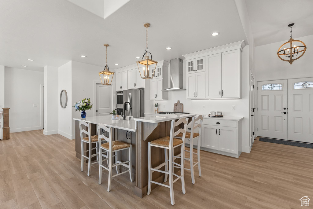 Kitchen with pendant lighting, wall chimney range hood, light hardwood / wood-style floors, white cabinetry, and stainless steel fridge with ice dispenser