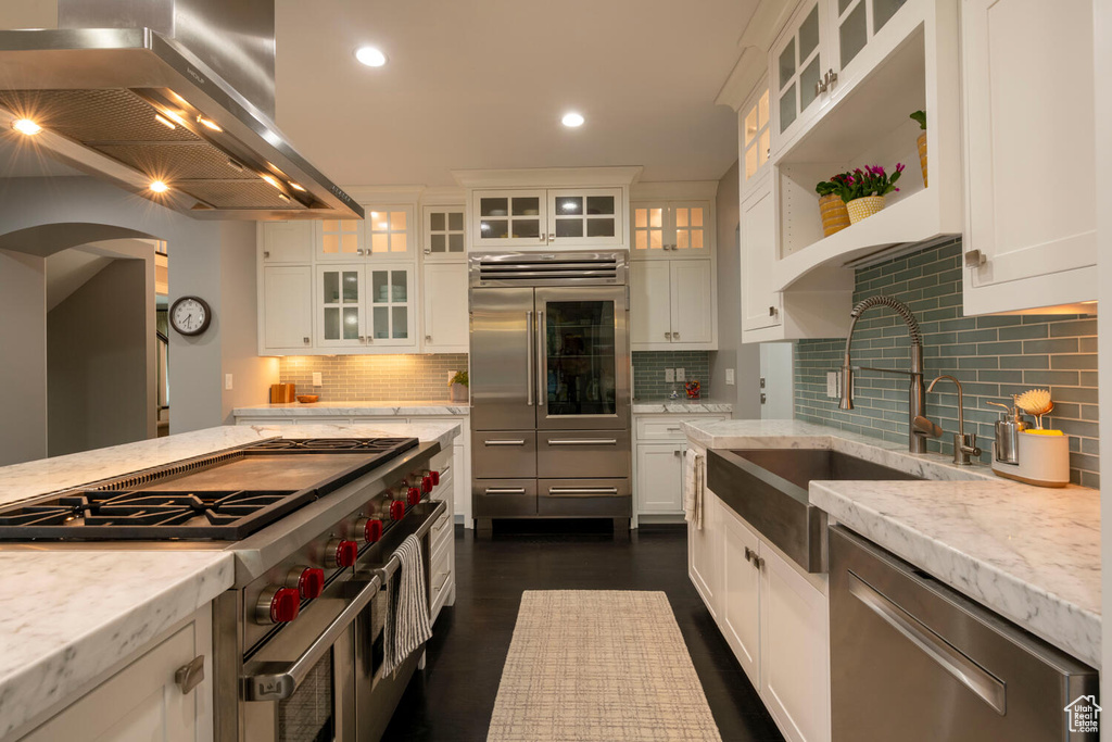 Kitchen with backsplash, white cabinets, island exhaust hood, and sink