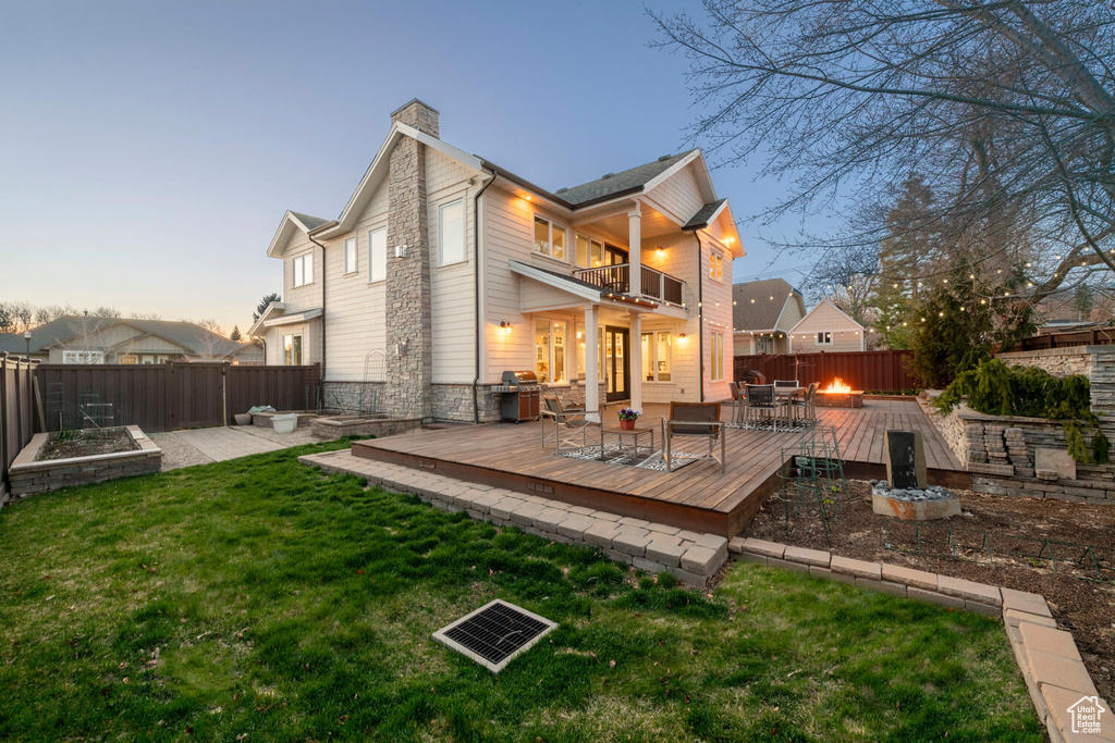 Back house at dusk with a patio, a lawn, a balcony, a deck, and an outdoor fire pit