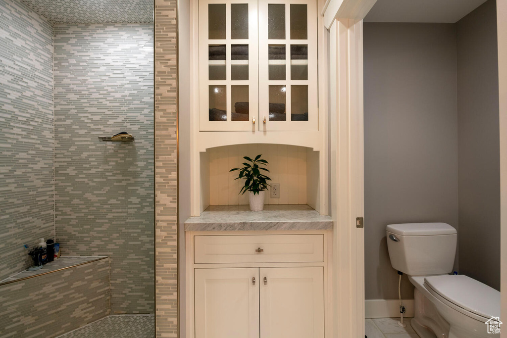 Bathroom featuring toilet, tile flooring, vanity, and tiled shower