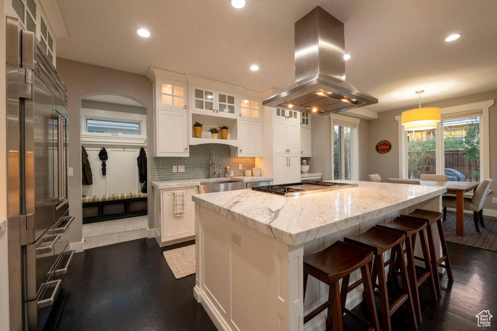 Kitchen featuring hanging light fixtures, white cabinets, a center island, island range hood, and tasteful backsplash
